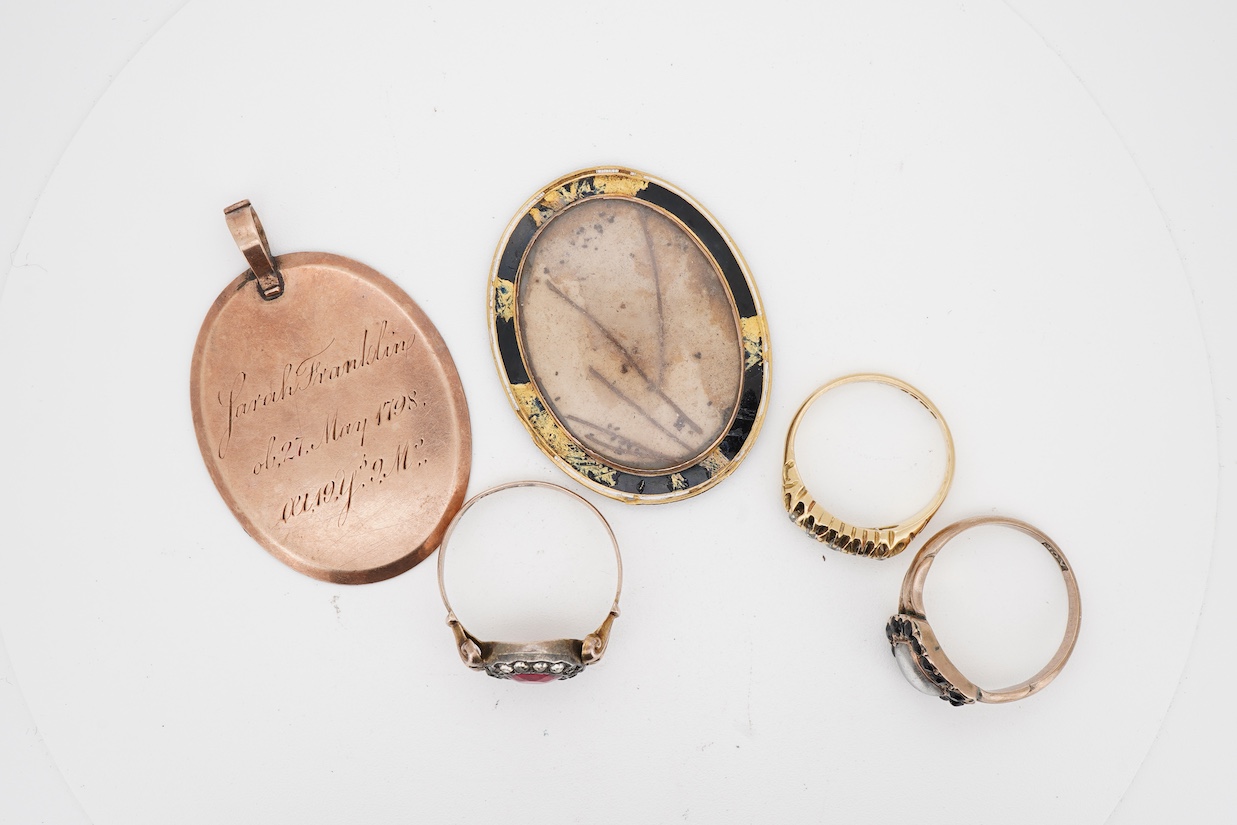 A George V 18ct gold and graduated claw set five stone diamond ring, size K, together with a 9ct and two colour paste set ring, a 19th century mourning ring, with plaited hair and an George III yellow metal and enamel mo